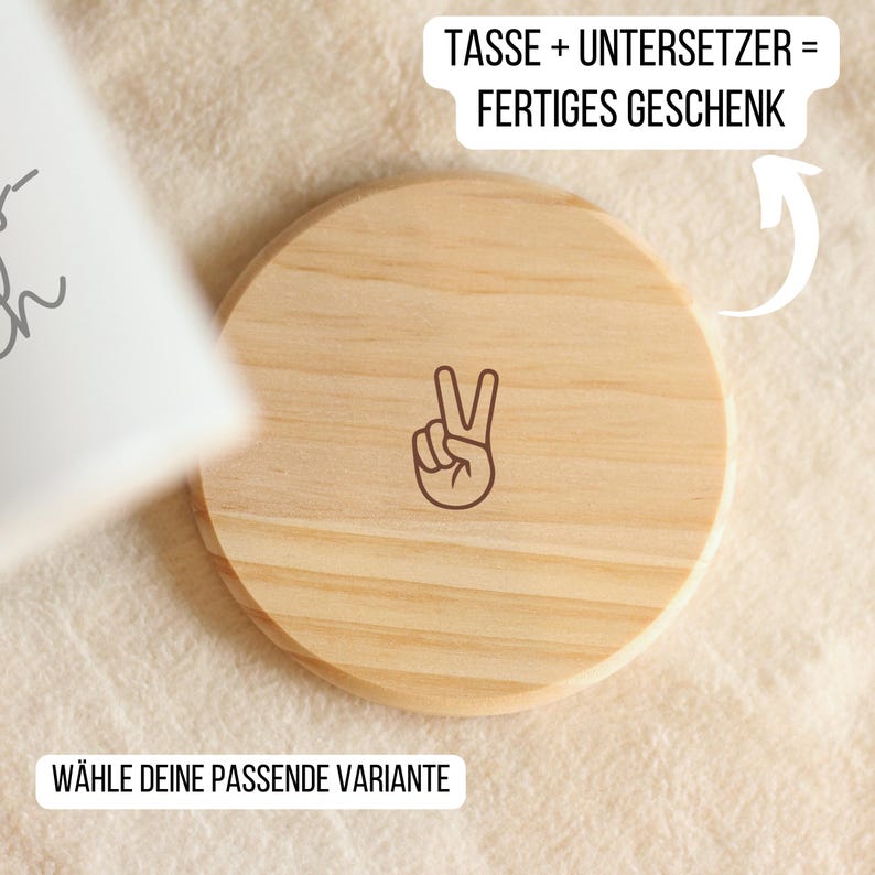 May include: A round, light-colored wooden coaster with a peace sign graphic. The coaster has a natural wood grain pattern and is shown on a textured, off-white surface. Text in German reads "TASSE + UNTERSETZER = FERTIGES GESCHENK" and "W&Auml;HLE DEINE PASSENDE VARIANTE".