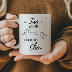 Könnte beinhalten: Weiße Keramiktasse mit einem schwarzen Design mit zwei singenden Vögeln mit Noten und dem Text "Der Tag ist Gerettet Ich Habe Heute Chor".