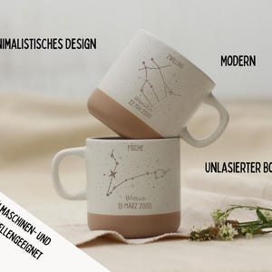 May include: Two stacked white ceramic mugs with speckled finish and tan bases. Each mug features a constellation design and text. The mugs are labeled "Zwillling" and "Fische". The text "Minimalistisches Design", "Modern", and "Sp&uuml;lmaschinen- und Mikrowellengeeignet" are also visible.
