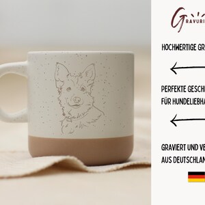 May include: A speckled ceramic mug with a cream-colored handle and upper half, and a tan-colored lower half. The mug features a detailed line drawing of a dog's face. The text on the right side says "Hochwertige Gravur" and "Perfekte Geschenk f&uuml;r Hundeliebhaber."