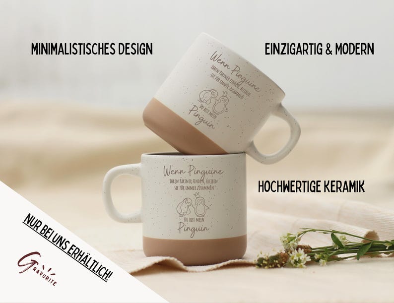 Puede incluir: Dos tazas de cer&aacute;mica blanca con un acabado moteado y bases marrones apiladas. Cada taza presenta una ilustraci&oacute;n de ping&uuml;ino y texto en alem&aacute;n. Las tazas tienen un dise&ntilde;o minimalista y est&aacute;n hechas de cer&aacute;mica de alta calidad.