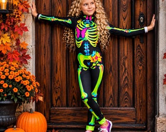 May include: A black long-sleeve jumpsuit featuring a neon green skeleton print with a pink butterfly on the chest and a yellow flower on the hip. The jumpsuit has a high neckline and is paired with a large, multi-colored rainbow hair bow.