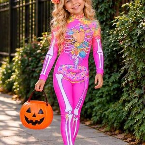 May include: A bright pink long-sleeve jumpsuit featuring a white skeleton print on the arms and legs, with a colorful graphic of a heart and donuts on the torso. The outfit is paired with a floral crown and an orange plastic jack-o'-lantern bucket.
