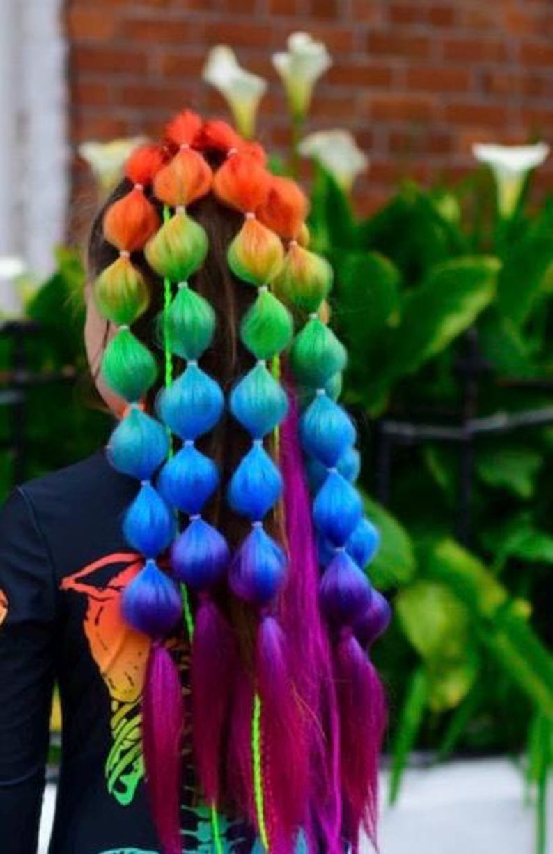 May include: A hairstyle featuring multiple sections of hair tied into bubble ponytails with a vibrant rainbow gradient color scheme, transitioning from red and orange at the top to green, blue, and purple at the ends, with loose magenta hair strands.