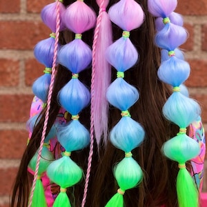May include: A hair accessory featuring multiple long strands of synthetic hair in a gradient of pink, purple, blue, and green. The hair is styled into bubble braids secured with small neon green elastic bands, with thin braided accents.