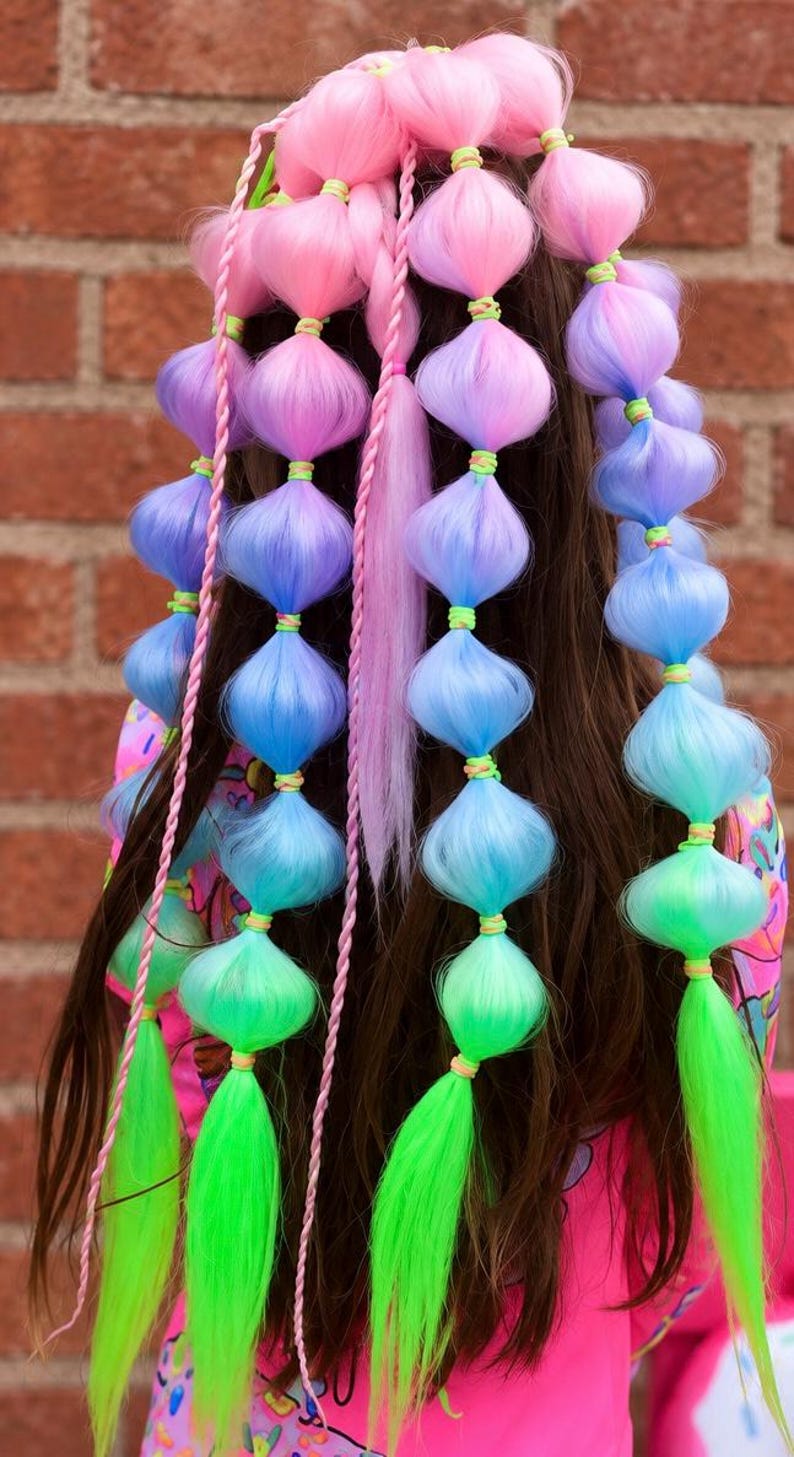 May include: A hair accessory featuring multiple long strands of synthetic hair in a gradient of pink, purple, blue, and green. The hair is styled into bubble braids secured with small neon green elastic bands, with thin braided accents.