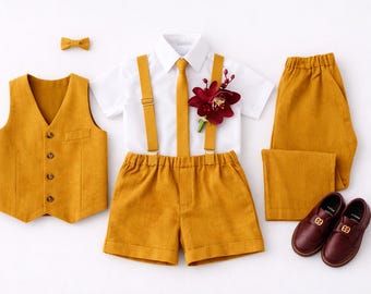 May include: A mustard yellow formal outfit for a child, including a vest, shorts, suspenders, a bow tie, a white shirt, and matching shoes. The outfit is accented with a burgundy flower and is arranged on a white surface.