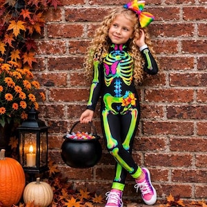 May include: A black long-sleeved jumpsuit featuring a neon-colored skeleton print with a pink butterfly and orange flowers on the chest and hip. The outfit includes a large, multi-colored rainbow hair bow and pink and white lace-up sneakers.
