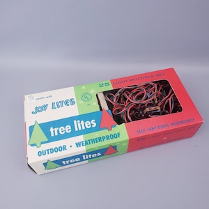 May include: A rectangular cardboard box containing a 25 light multiple set of Joy Lites. The packaging is white, green, and red with text reading "Joy Lites," "tree lites," "outdoor weatherproof," and "each lamp burns independently" with tree graphics.