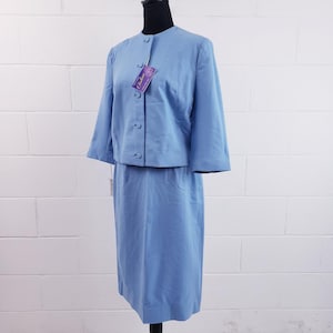 Könnte beinhalten: Hellblauer Hosenanzug mit passendem Blazer. Der Blazer hat Dreiviertelärmel und Knopfverschlüsse. Ein Etikett ist am Blazer befestigt. Der Rock ist knielang. Der Anzug wird auf einer schwarzen Schaufensterpuppe präsentiert.