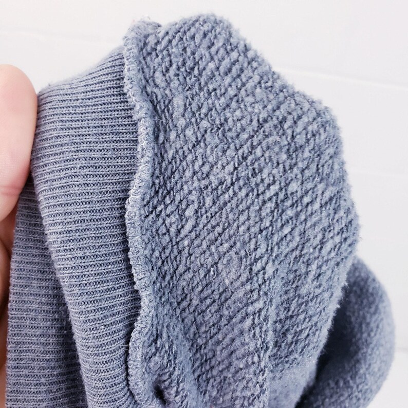 Puede incluir: Primer plano de una tela azul, que muestra dos texturas distintas. Un lado presenta un punto acanalado, mientras que el otro tiene un aspecto texturizado y rizado. Los bordes est&aacute;n cuidadosamente cosidos, resaltando el contraste entre los materiales.