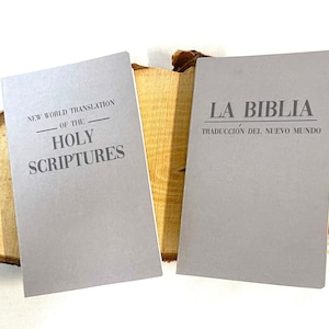 Può includere: Due libri tascabili grigi con i titoli "New World Translation of the Holy Scriptures" e "La Biblia Traducción del Nuevo Mundo".