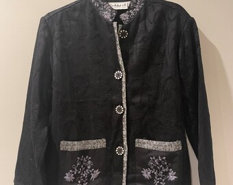 May include: A black embroidered jacket with a mandarin collar and silver buttons. The jacket has two pockets with embroidered floral designs and a "Flashback" label on the collar.