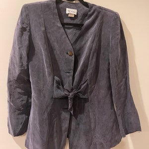 May include: A gray suede blazer with a bow tie detail at the waist. The blazer has a single button closure and long sleeves.