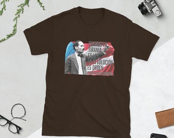 May include: Brown t-shirt with a graphic of a man in a suit and a quote in Spanish that reads "Cuando la tiranía es ley, la revolución es orden. Pedro Albizu Campos."