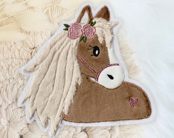 May include: A brown and white embroidered horse head patch with a pink flower crown and a pink heart on the cheek.