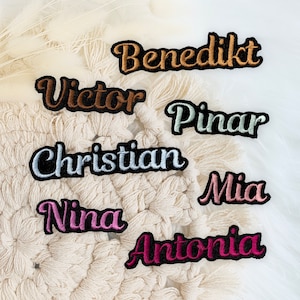 Könnte beinhalten: Ein Set mit sieben bestickten Bügelbildern in verschiedenen Farben. Die Namen sind: Benedikt, Victor, Pinar, Christian, Mia, Nina und Antonia.