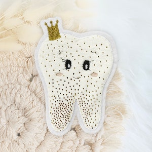 Könnte beinhalten: Ein weißer Filzzahn mit einer goldenen Krone und einem lächelnden Gesicht. Der Zahn ist mit goldenen Glitzerpunkten verziert.