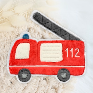 Könnte beinhalten: Roter Filz-Feuerwehraufkleber mit einer schwarzen Filzleiter, weißen Filzfenstern und der in Weiß gestickten Nummer 112.