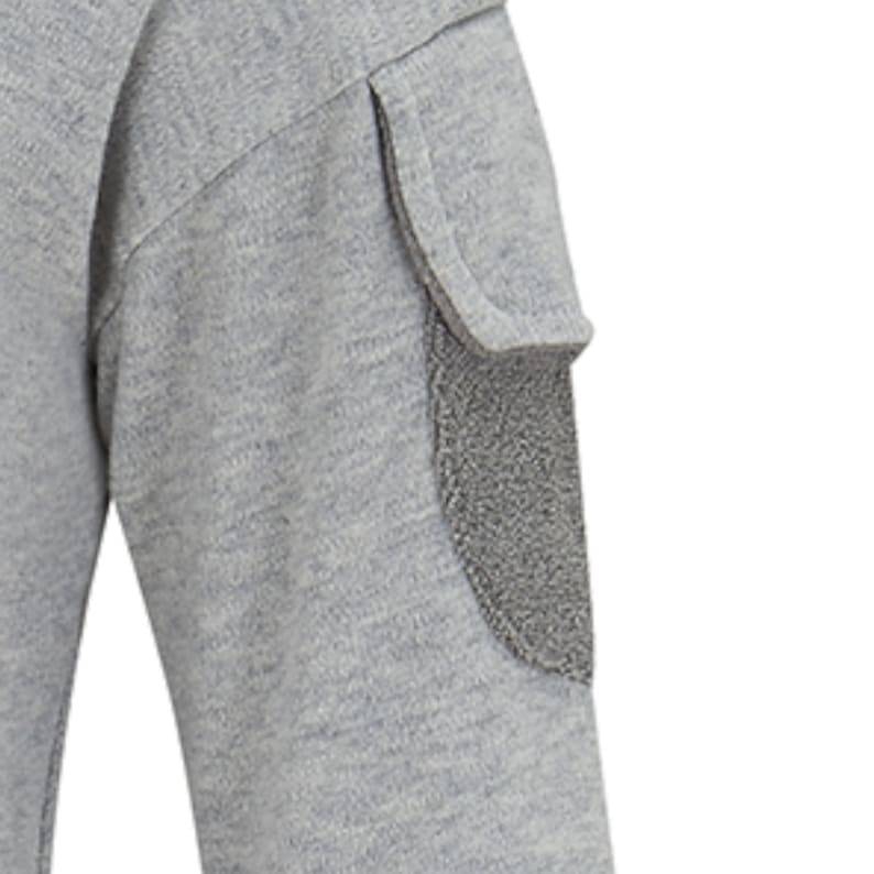 Puede incluir: Primer plano de una camisa gris de manga larga con un parche en el codo texturizado. El parche es de un tono gris m&aacute;s oscuro y tiene una textura borrosa. La tela de la camisa parece ser un material de punto suave.