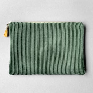 Könnte beinhalten: Eine grüne Cord-Clutch mit goldenem Reißverschluss und gelbem Quastenanhänger. Die rechteckige Tasche hat vertikale Rippen und ein schlichtes Design. Ein stilvolles Accessoire für wichtige Dinge.