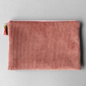 Könnte beinhalten: Eine rosa und braune Cord-Clutch mit Reißverschluss und goldener Quaste.
