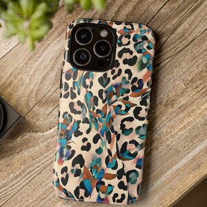 May include: A phone case with a colorful leopard print design. The case features a cream background with black spots and accents of blue, teal, and brown. The phone case has a camera module with multiple lenses.