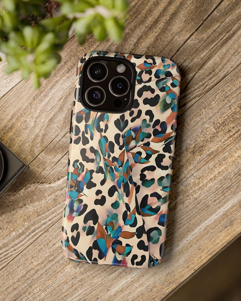 May include: A phone case with a colorful leopard print design. The case features a cream background with black spots and accents of blue, teal, and brown. The phone case has a camera module with multiple lenses.