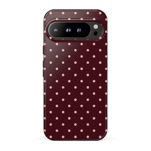 Puede incluir: Una funda para smartphone de color granate oscuro con un patrón repetitivo de pequeños lunares de color rosa claro. La funda incluye un recorte horizontal para la cámara en la parte superior, mostrando tres lentes circulares y un flash.