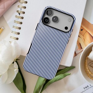 May include: A smartphone case featuring a vertical navy blue and white pinstripe pattern. The case has a rectangular cutout at the top for the camera lenses and flash, with a slim black border visible along the side edges of the device.