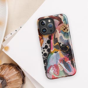 May include: A smartphone case featuring an abstract design with a mix of black, white, pink, blue, and tan colors. The pattern includes organic shapes, dotted textures, and fine line details across the entire surface of the rectangular cover.