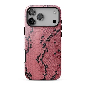 Può includere: Una custodia per smartphone con un motivo a pelle di serpente rosa e nero. Il retro della custodia presenta una texture a scaglie esagonali ripetute con macchie scure. La parte superiore include un ritaglio per un sistema a tripla fotocamera.