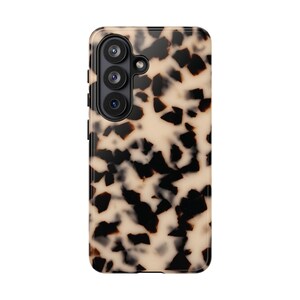 May include: A rectangular smartphone case featuring a tortoiseshell pattern with irregular black and dark brown spots set against a creamy beige background. The case includes a black camera module with three circular lenses and a small flash.