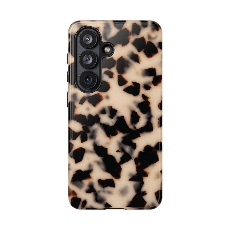 May include: A rectangular smartphone case featuring a tortoiseshell pattern with irregular black and dark brown spots set against a creamy beige background. The case includes a black camera module with three circular lenses and a small flash.