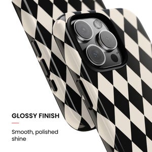 May include: A smartphone case featuring a black and cream harlequin diamond pattern with a glossy finish. The case has a smooth, polished shine and includes cutouts for the camera lenses and side buttons on the device frame.