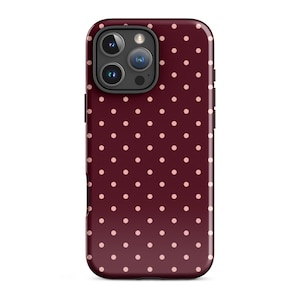 May include: A smartphone case featuring a deep burgundy background with a repeating pattern of small, light pink polka dots. The case has a cutout at the top left corner for a triple-lens camera system and a flash, with black side buttons visible.