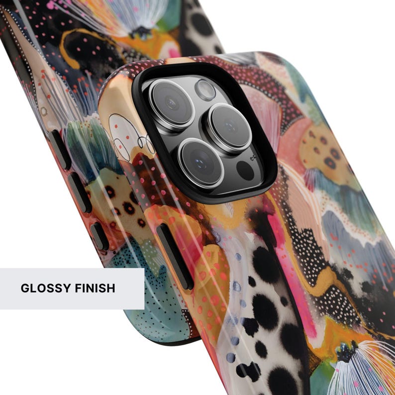 May include: A smartphone case with a glossy finish featuring an abstract, multi-colored pattern of black spots, pink dots, and flowing shapes in shades of orange, blue, and white. The case has a black camera cutout and black side buttons.
