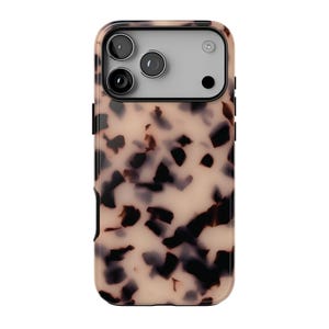 Op de afbeelding: Een beschermend telefoonhoesje met een beige en donkerbruin schildpadpatroon. Het bovenste gedeelte bevat een rechthoekige uitsparing voor een drievoudig camerasysteem met een lichtgrijze achtergrond, drie ronde lenzen en een kleine flitser.