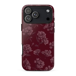 May include: A smartphone case in a deep burgundy color featuring a repeating pattern of dark floral illustrations. The case has a black camera module cutout at the top with three circular lenses and a flash, maintaining a sleek, uniform design.