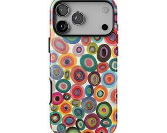 以下が含まれることがあります： マルチカラーの同心円が描かれた鮮やかで抽象的なパターンのスマートフォンケース。クリーム色の背景に、赤、オレンジ、黄色、緑、青、紫の色合いの重なり合うリングがデザインされています。