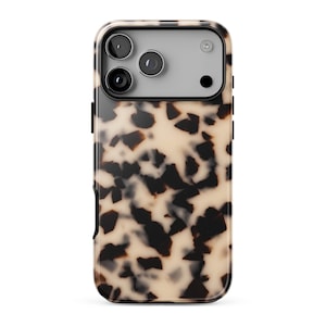 May include: A smartphone case featuring a classic tortoiseshell pattern with irregular dark brown and black spots set against a creamy beige background. The case includes a rectangular cutout at the top for a triple camera system and flash.