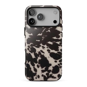 May include: A smartphone case featuring a black and cream-colored cow print pattern. The case has a rectangular cutout at the top for the camera lenses and flash, with a light gray border surrounding the camera module area on the back of the phone.