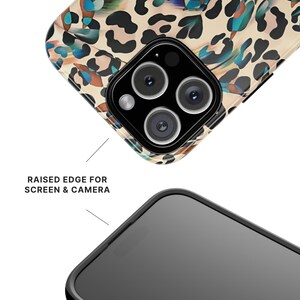 May include: A phone case with a leopard print design in tan, brown, and teal. The case has a raised edge for screen and camera protection. The phone's camera lenses are visible.