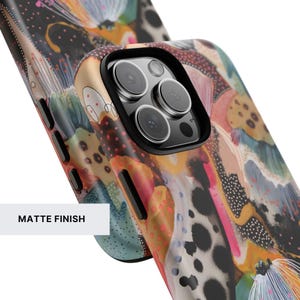 May include: A phone case with a matte finish featuring an abstract, multi-colored pattern of black spots, pink dots, and flowing shapes in shades of orange, blue, and green. The case has a black camera cutout and black side buttons.