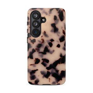 May include: A rectangular smartphone case featuring a beige and cream background with an irregular, scattered pattern of dark brown and black tortoise shell-like spots. The case includes a vertical camera cutout with three lenses.
