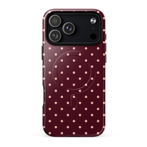 May include: A burgundy phone case with a repeating pattern of small, light pink polka dots. The case has a glossy finish and a camera cutout for a triple-lens camera system. The case has a magnetic charging circle on the back.