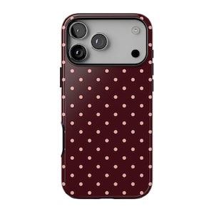 May include: A smartphone case featuring a deep burgundy background with a repeating pattern of small, light pink polka dots. The upper section includes a rectangular cutout for a triple-lens camera system and a flash, framed in black.