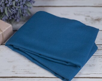 May include: A folded piece of blue fabric with a textured surface. The fabric is folded in thirds and is lying on a white wooden surface.