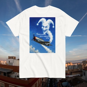 May include: White t-shirt with a graphic of a vintage aircraft in a blue sky, accompanied by a smiling cloud figure and the text "Lovely weather you've engineered today."