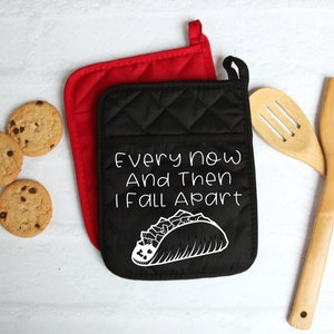 May include: Black and red quilted oven mitts with the text "Every now and then I fall apart" and a white outline of a taco with fillings.